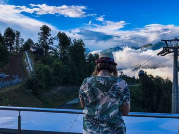 Rear view of people standing by trees against sky