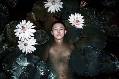 Portrait of shirtless man floating amidst flowers and leaves in lake