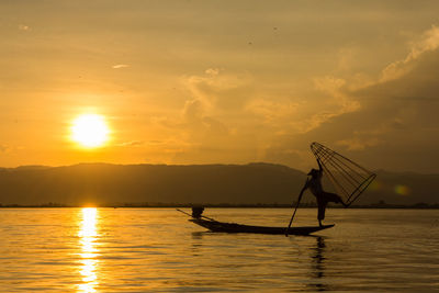 Silhouette people sailing in lake against sky during sunset