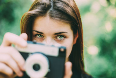 Close-up portrait of woman holding camera outdoors