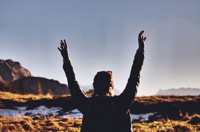 Rear view of woman with arms raised standing on field against clear sky