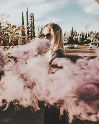 Woman wearing sunglasses while standing amidst smoke