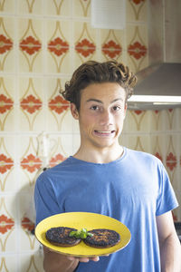 Portrait of boy making face while holding burn food in plate at home