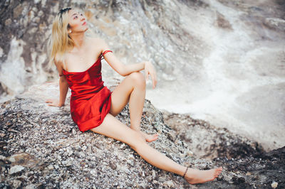 Sensuous woman in red dress sitting on rock
