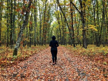 Back of woman wearing black tracksuit standing alone in the middle of the forest in autumn