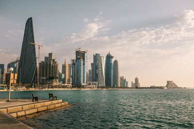 Contemporary skyscrapers located on coast of rippling sea against cloudless sundown sky in evening in doha, qatar