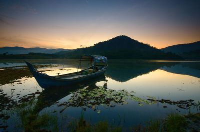 Boat moored in lake against sky during sunset