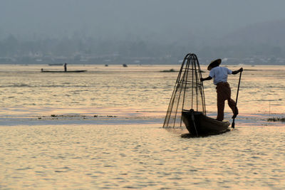 Rear view of man fishing in lake at sunset