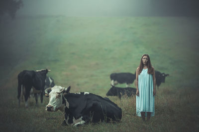 Portrait of woman standing with cows on field during foggy weather