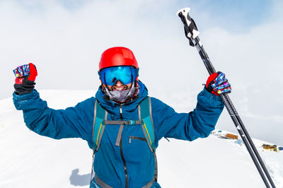 Young man standing in snow with raised hands and ski poles, joy and happiness on the face of the guy