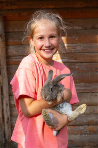 A smiling child holding a cute gray rabbit looking at camera