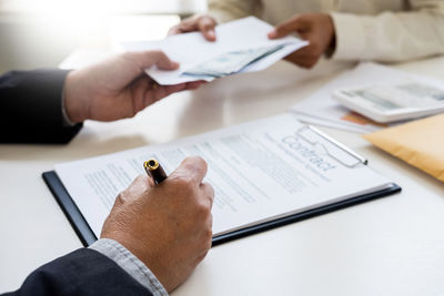 Close-up of man holding paper with pen on table