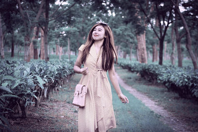 Young smiling woman looking away while standing against trees