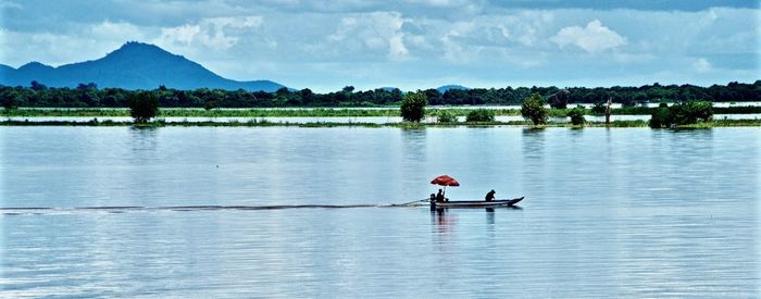 Men in boat on lake against sky