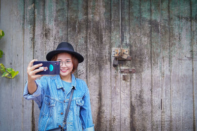 Woman taking selfie while standing against wood