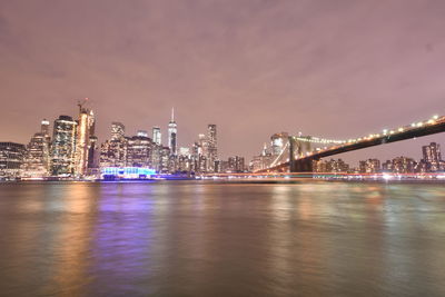 Illuminated bridge over river with buildings in background at night