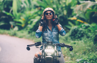 Woman wearing helmet while sitting on motorbike on road