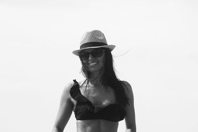 Portrait of smiling young woman wearing sunglasses standing against clear sky