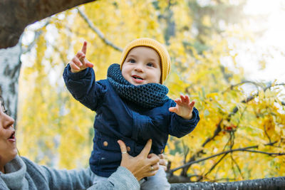 Midsection of woman carrying happy toddler son against autumn tree