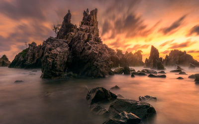 Rock formation in sea against sky during sunset