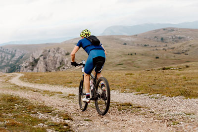 Rear view of man riding bicycle on field