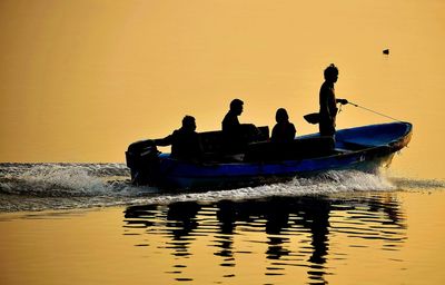Silhouette people in little motor boat at sunset