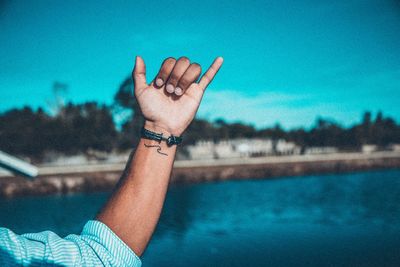 Close-up of human hand on water against sky