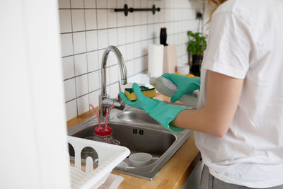 Midsection of young woman cleaning utensils while standing at home