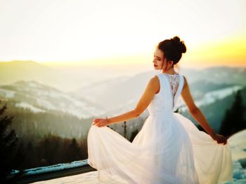 Woman with arms raised against sky during sunset