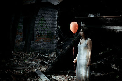 Woman holding helium balloon while standing at forest