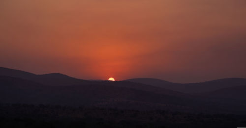 Scenic view of silhouette mountains against orange sky