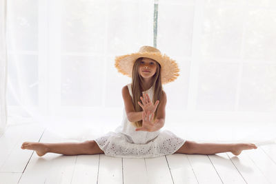 Girl in a white dress in a straw hat sitting on a twine on the white floor in the room