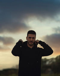 Portrait of young man standing against sky during sunset