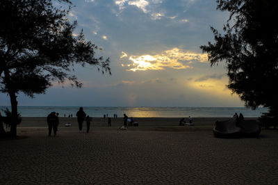 Silhouette people on beach against sky during sunset