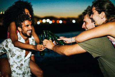 Friends toasting drink against sky during sunset