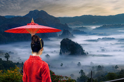 Rear view of woman with red umbrella on mountain against sky