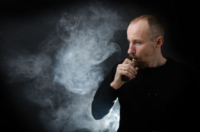 Man smoking electronic cigarette against black background