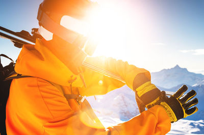 Young unrecognizable man holds skis on his shoulder in bright clothes, gloves and a ski mask