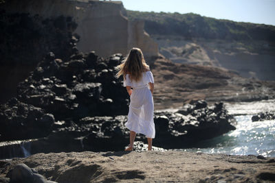 Rear view of woman standing on rock at beach