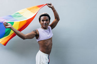 Happy man with rainbow flag standing against wall