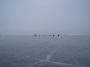 People on frozen sea against clear sky during winter