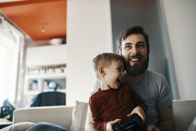 Father and son sitting together on the couch playing computer game