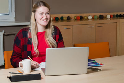 Cheerful businesswoman using laptop while sitting at table in office