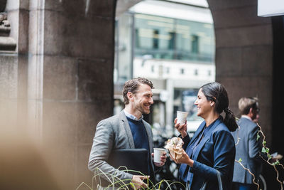 Happy business people with coffee standing at sidewalk cafe