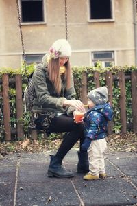 Baby boy drinking fruit juice with mother in park in a cold day