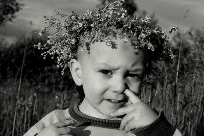 Portrait of boy wearing flower wreath while picking nose on field