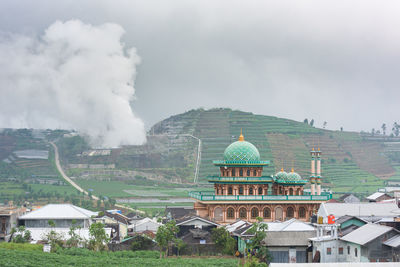 Village mosque, rice field and toxic smokes of sulfur extraction plant, in dieng, java, indonesia