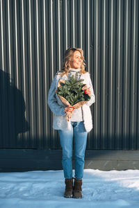 Portrait of woman in winter clothes with fir branches in hands against background of grey wall