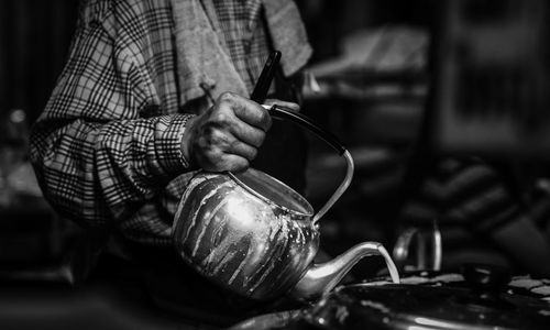 Midsection of man pouring drink from teapot in commercial kitchen