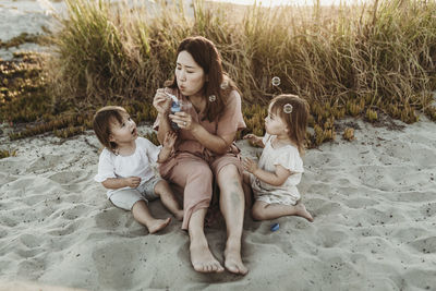 Mother with young twin daughters blowing bubbles at the beach